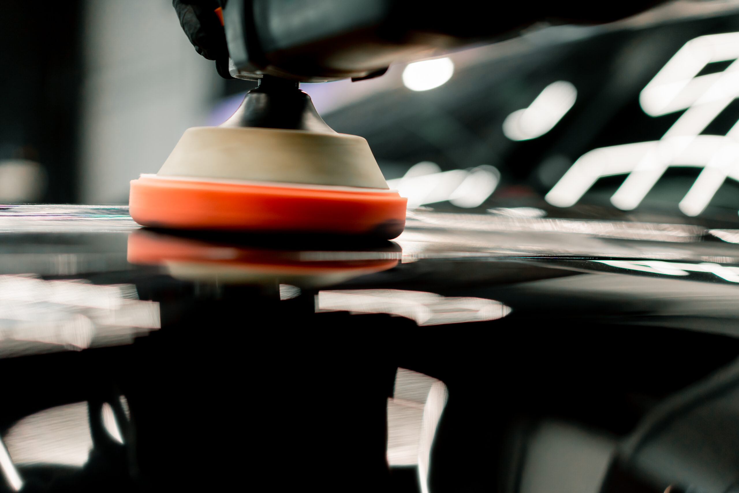 close up of a car wash worker using a polishing machine to polish the hood of black luxury car